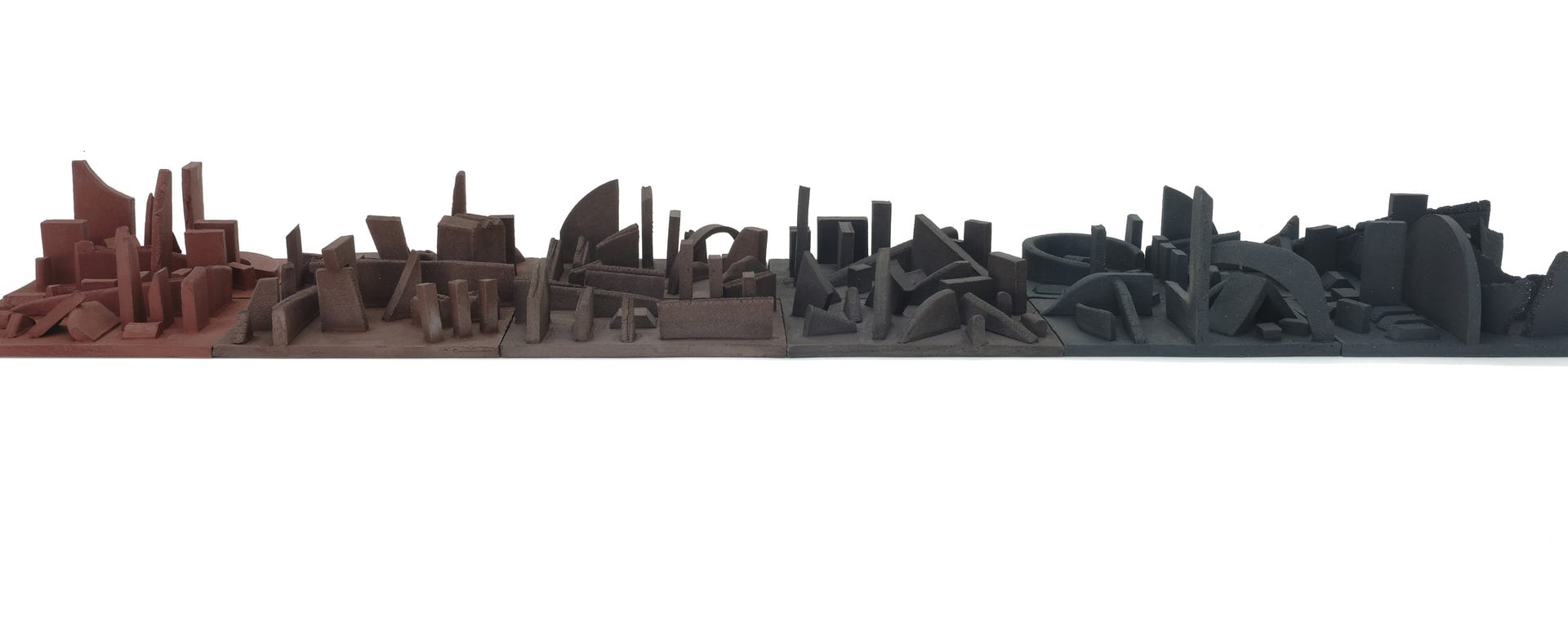 A set of tiles that fit together as parts of a cityscape in clay that graduates from red through to black