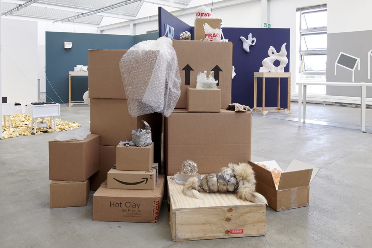 Piles of cardboard boxes in the middle of a room supporting objects in glass