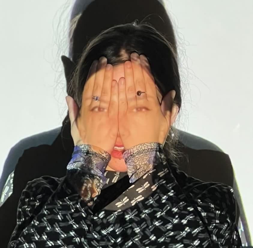 a close portrait of a woman with her hands in front of her face, a projection of her face is visible on top of her hands