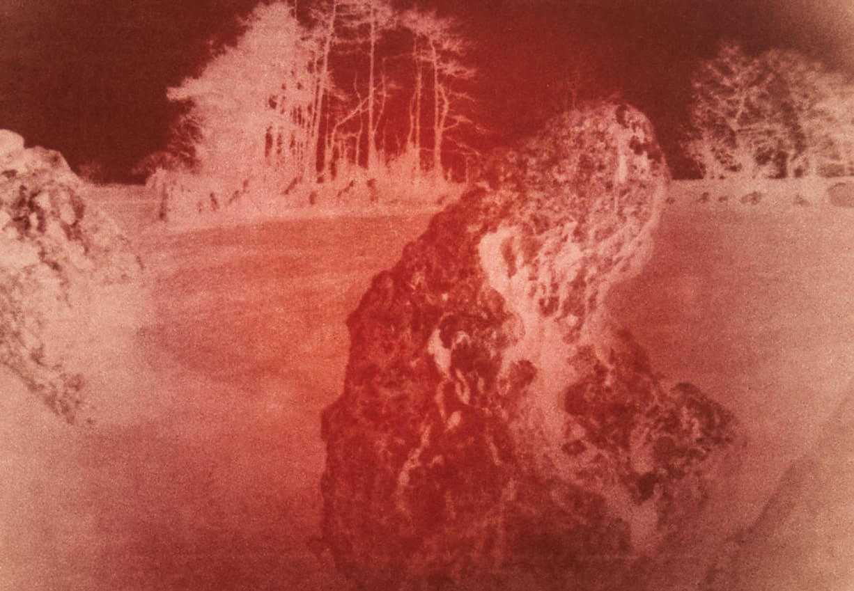 a large standing stone with tall trees in the background. The image is red in the centre blending out to brown.