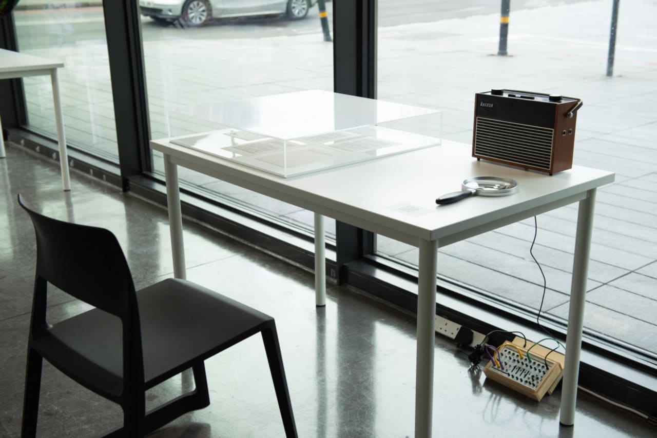 Autocrat, 1967, Mixed media - Sound (11’ endless tape loop), transistor radio, LFO radio signal, perspex box, paper, table, chair, magnifier