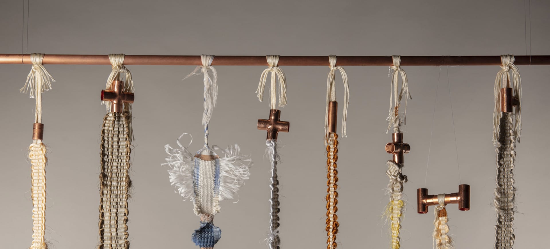 Six hand-woven sculptural strips that incorporate colourful thick silk wefts, suspended off copper pipes and fittings.