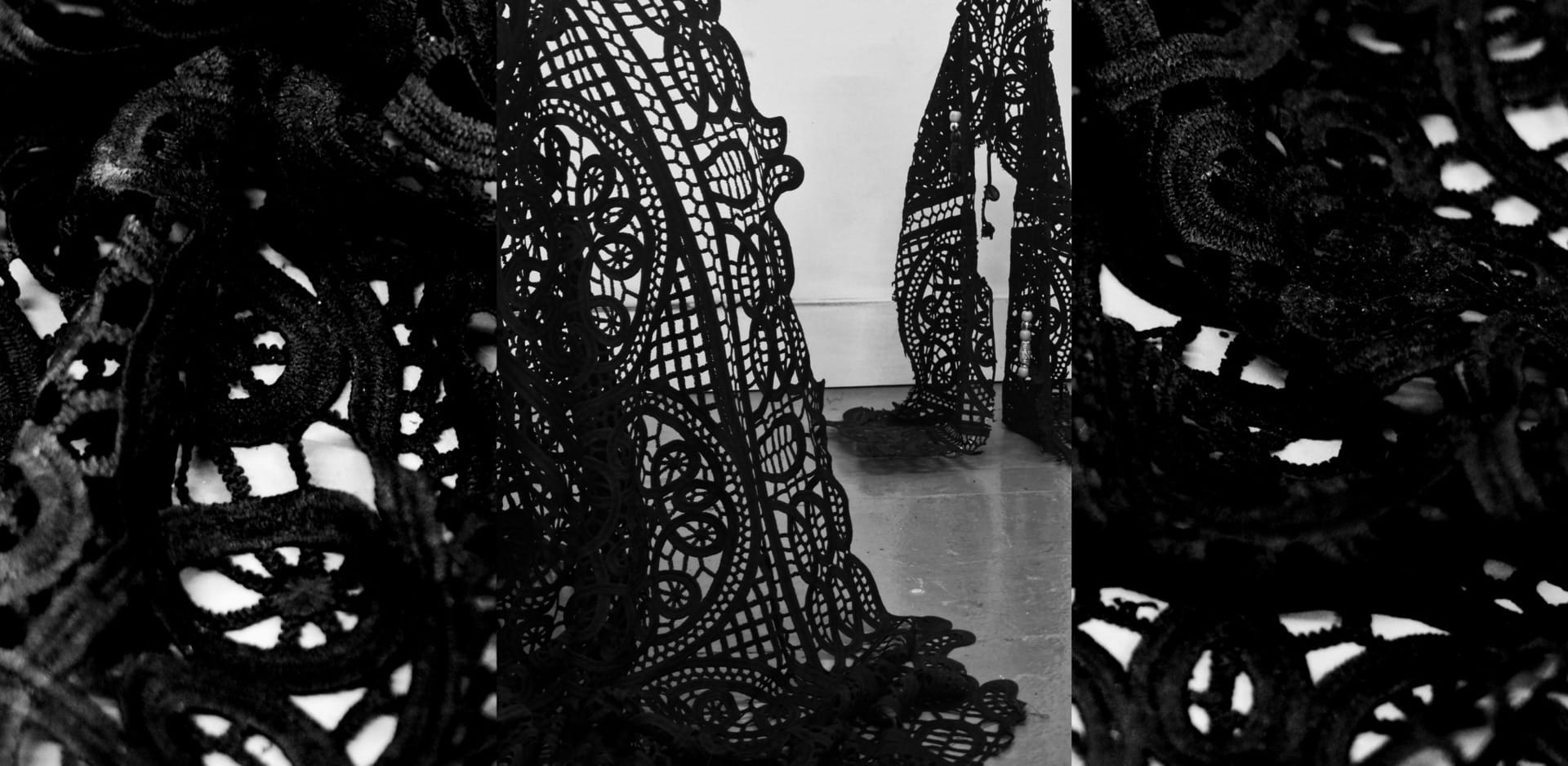 Two black lace sculptures, one standing close to a white wall while the other is cut off in the foreground.