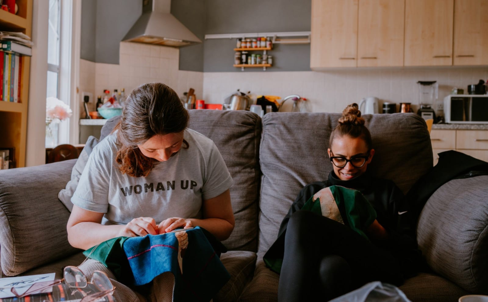 Two woman sewing, sat together on a sofa.