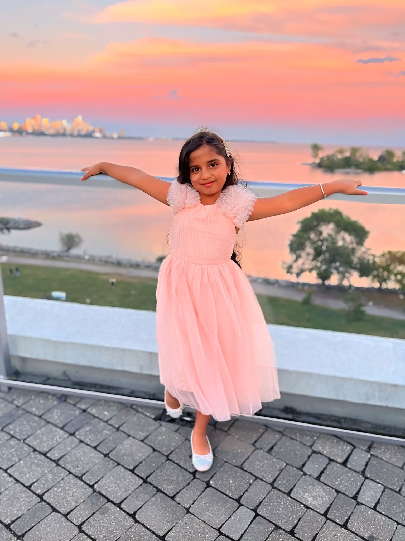 Natasha with her arms outstretched in a pink dress at sunset