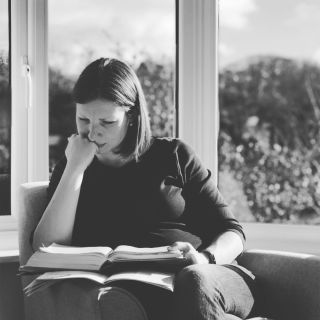 A woman sat reading a bible in a bay window