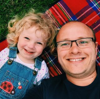 A child and her father laying on a picnic blanket