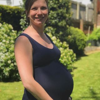 A pregnant woman standing holding her belly in a garden. 