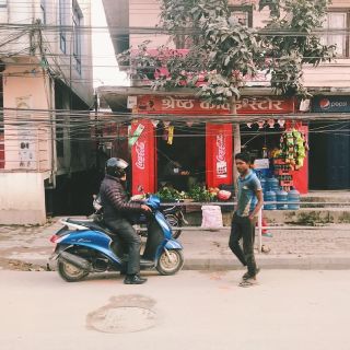 A man on a motorbike and a man walking in front of a nepalese shop front