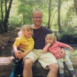 A dad and two girls sat on a log over a stream