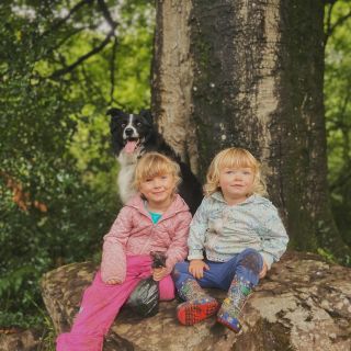 Two girls sat on a large rock with a border collie