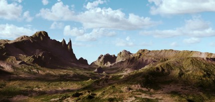 Landscape mountain terrain, patches of grass with cloudy blue sky.