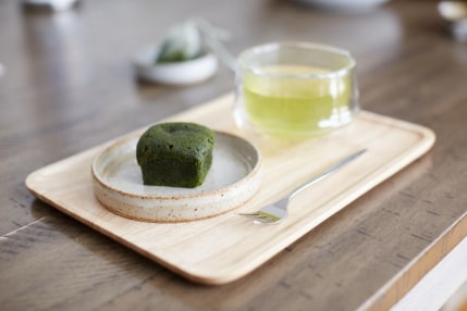 A wooden tray holding a dish with a matcha pastry and a cup of green tea.