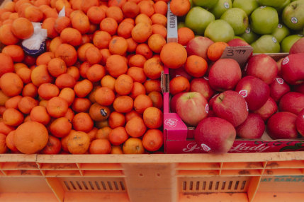 Colorful fruits at the farmers market. Orange tangerines, green apples and red apples in an orange box.