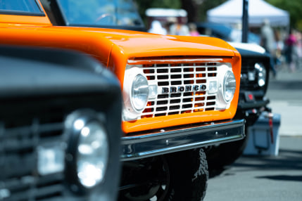 the front grill of an orange Bronco wedged between two black Broncos that are out of focus