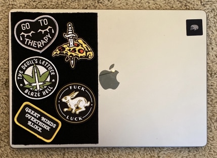 A MacBook with a Velcro adhesive patch on the left side of the cover, covered in Velcro patches