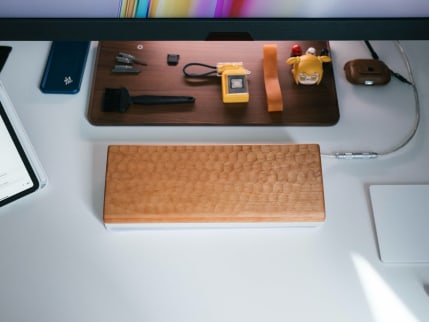 Plain white desktop with various items scattered around, including a wooden keyboard cover with turtle shell-like texture.