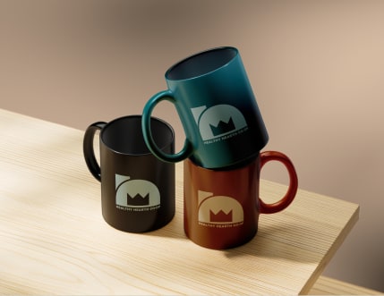 A photo of three coffee mugs. One black, one brown, one teal. They each have the logo for Healthy Hearth Coffee. The logo is made of a semicircle in front of a rectangle, with a three-pointed crown set inside.