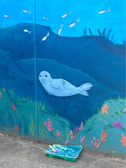 A baby seal painted on an underwater-themed community mural in Vancouver. Paint tray on ground.