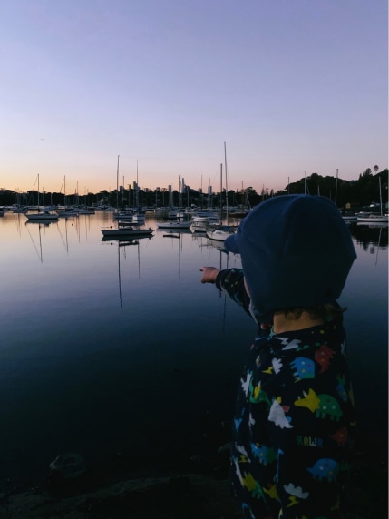 Kid pointing at boats in a bay during sunrise