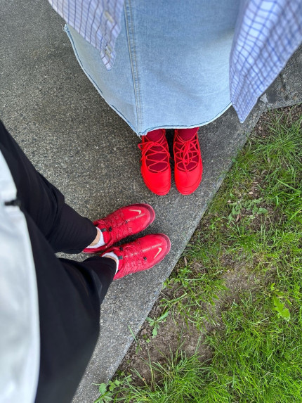 Two people wearing bright red shoes. One in black pants and the other in a jean skirt.