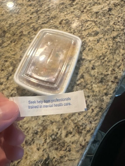 A person holding a fortunate from a fortune cookie that reads “seek help from professionals trained in mental health care”