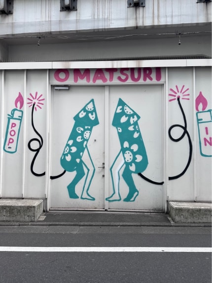 Mural of two firecrackers with legs. Their tails are lit fuses. Above them, it says “omatsuri”