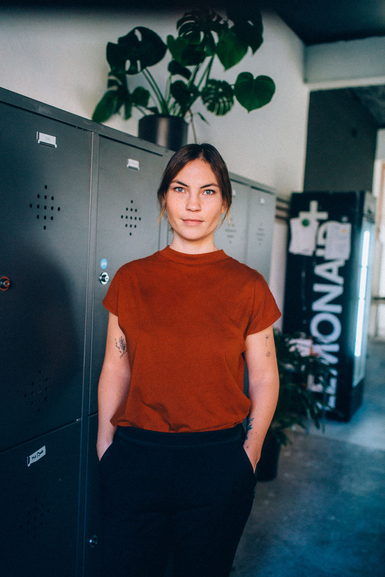Auf dem Bild ist unsere Head of HR Melanie Kremer zu sehen. Sie trägt ein rotes Shirt und steht vor einem schwarzen Spind im Büro.
