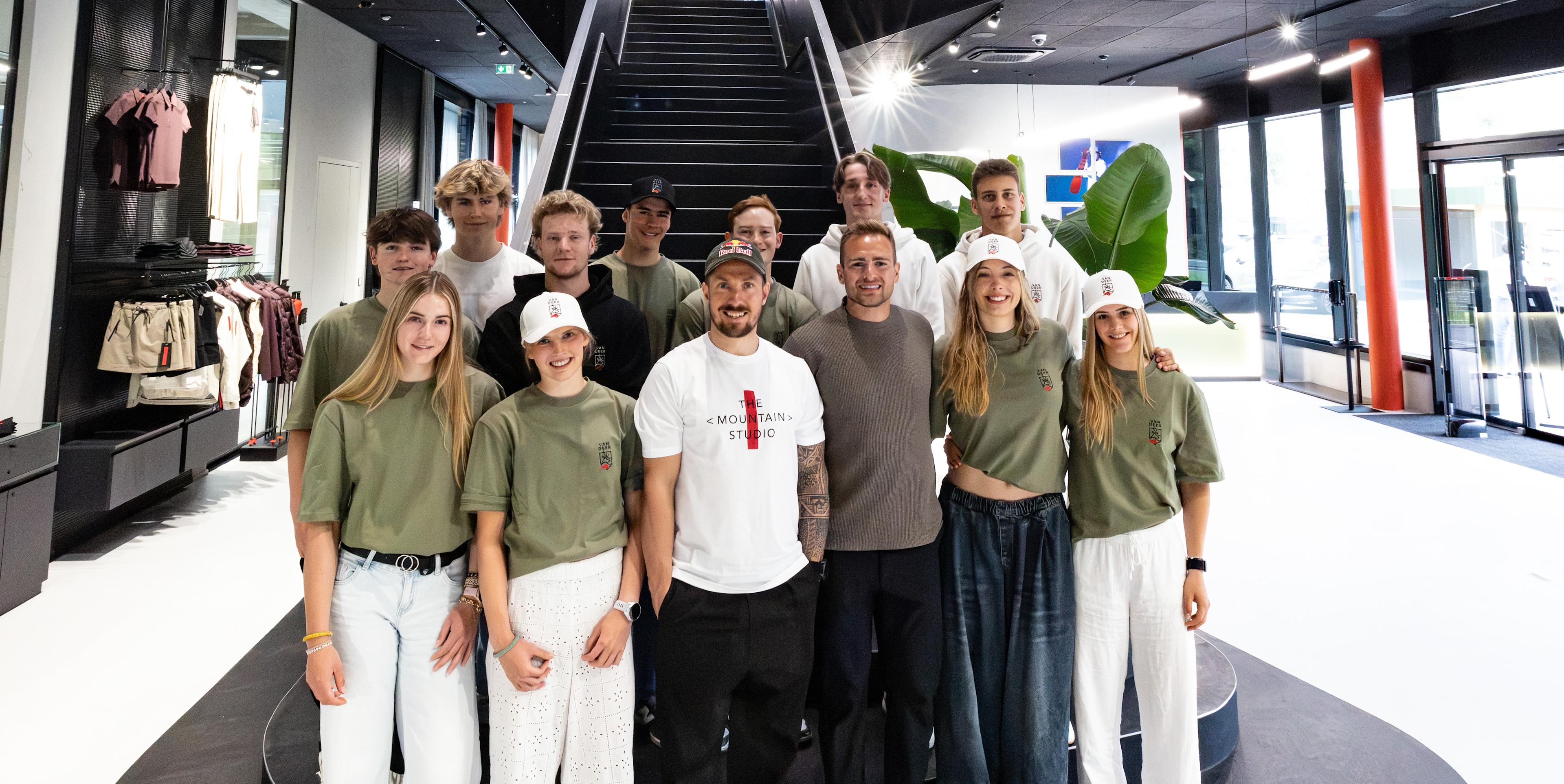 Marcel Hirscher und AJ Ginnis mit elf Nachwuchsathleten von VAN DEER-Red Bull Sports im Flagship Store vor einer Stiege.