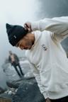 A man is wearing a black cap and a white VAN DEER-Red Bull Sports Essential Hoodie with the logo on the chest. He is looking down while one hand touches the brim of the cap.