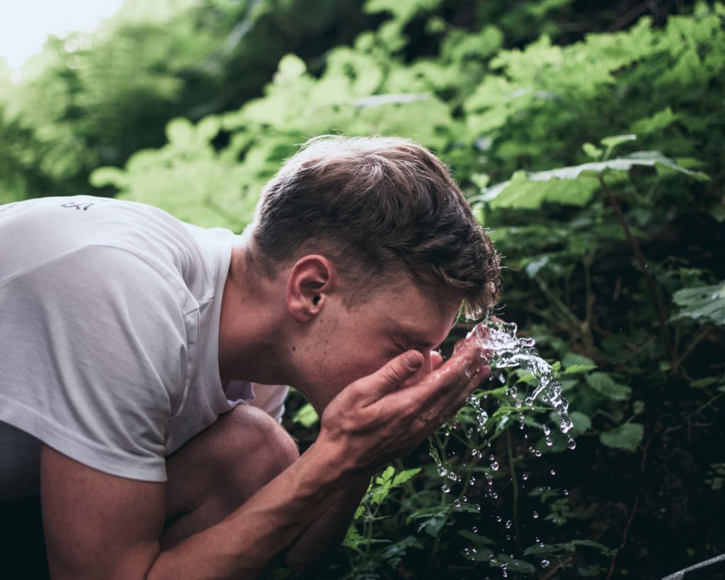 Man washing his face with fresh water in front of bushes