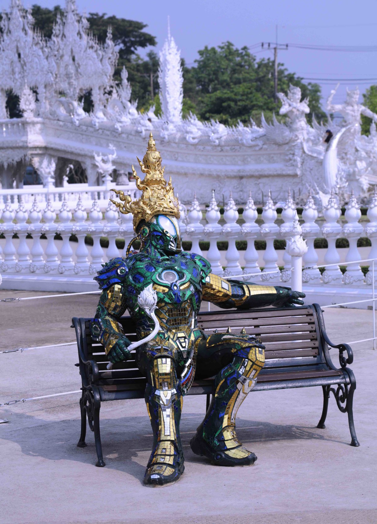 Life size robot statue sitting on a bench in front of the temple