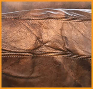 A Restoration Hardware backrest cushion showing cracking in areas stressed and creased from leaning back, highlighting lack of routine moisturizing. This couch needs our Leather Conditioning treatment.