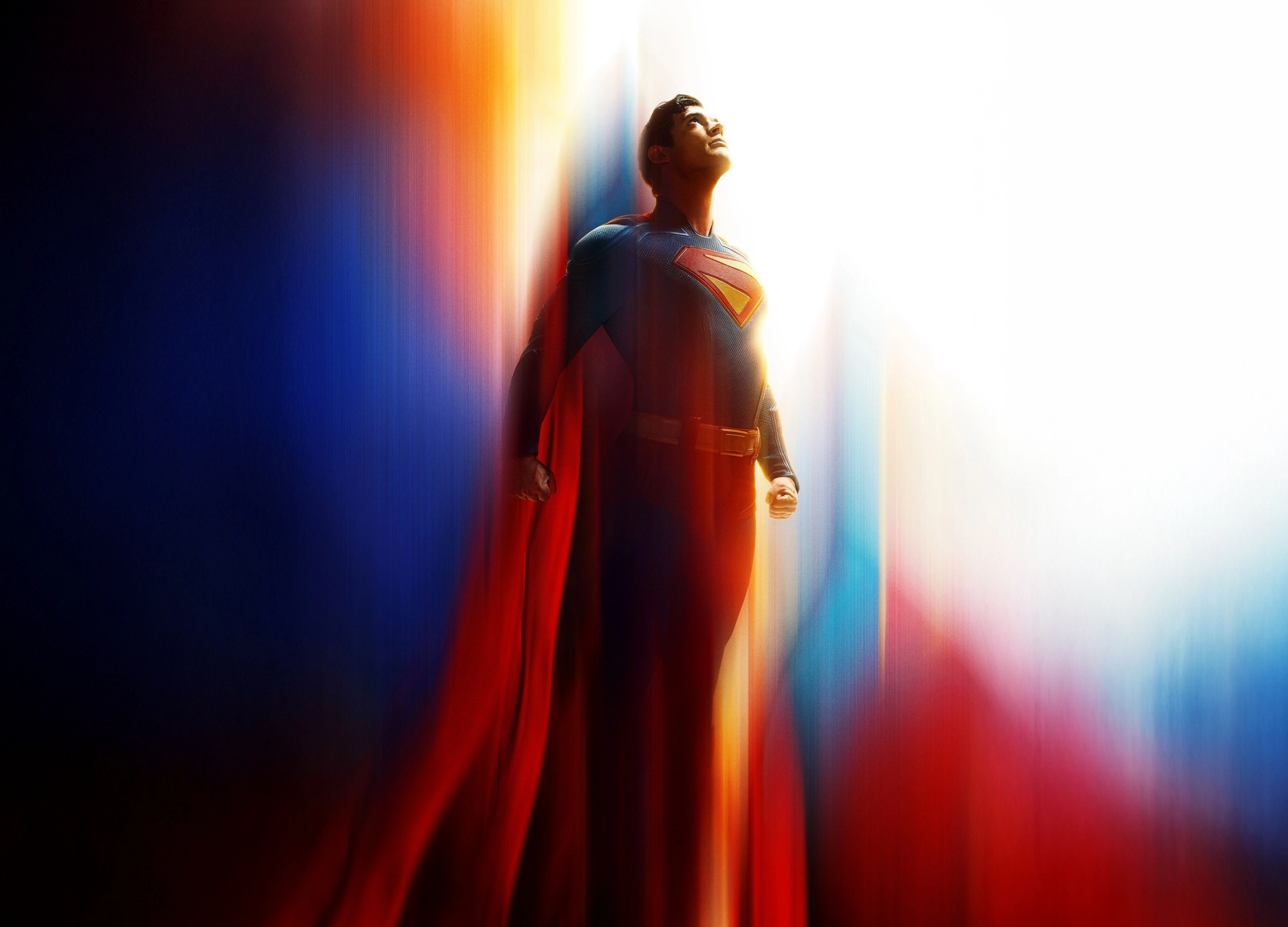 a full-body shot of a man in his suit and cape, looking upwards with a bright light behind him.
