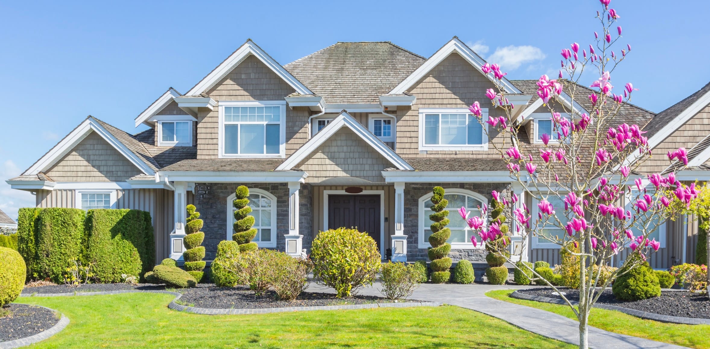 Grey house with green grass and a tree with pink flowers. Springtime
