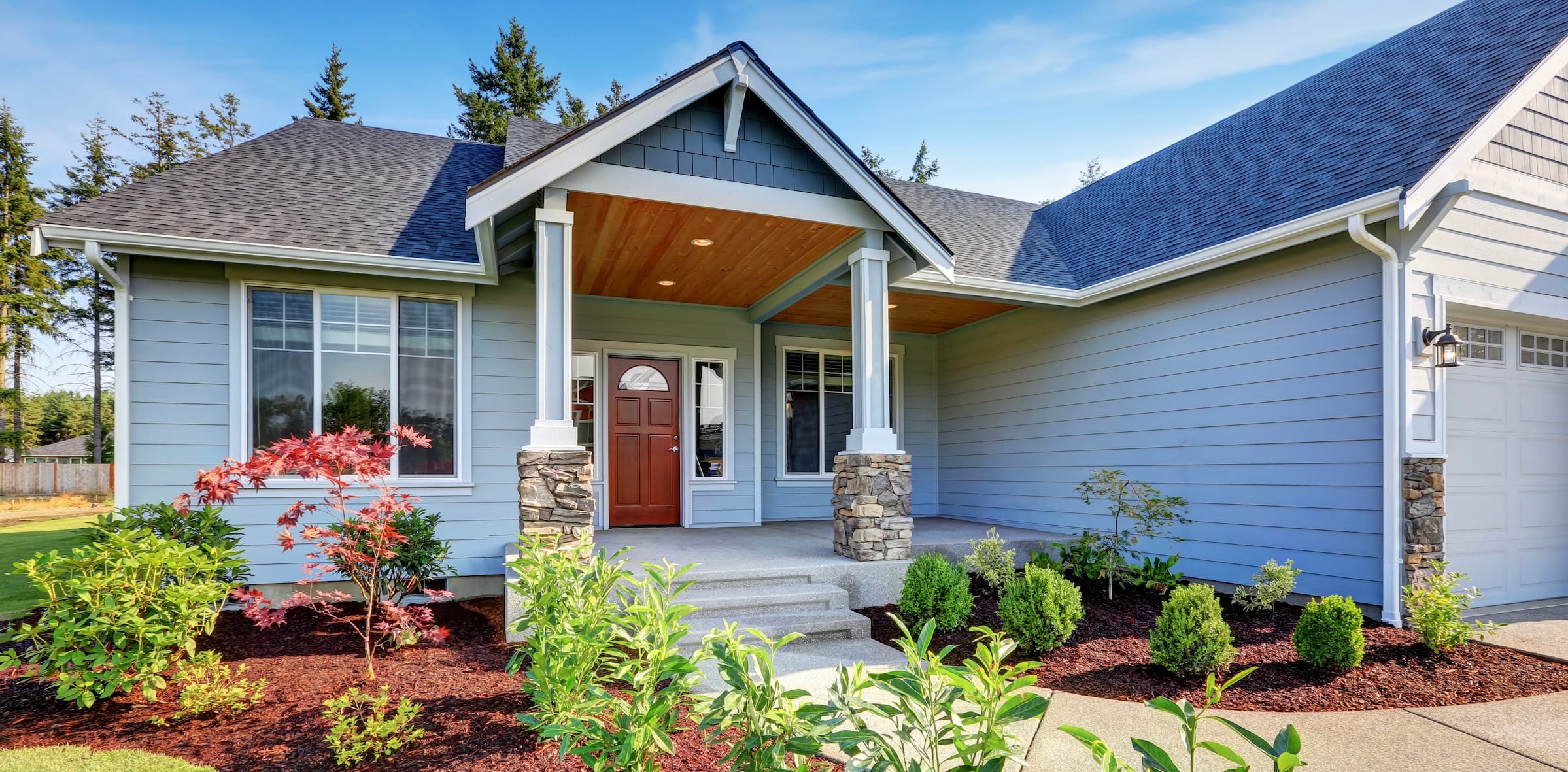 Blue house with a red front door and fresh landscaping.