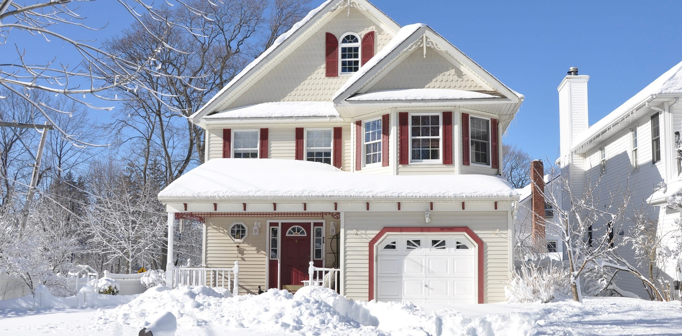 White house with maroon shutters and a maroon front door. There are blue skies and plenty of snow on the ground.