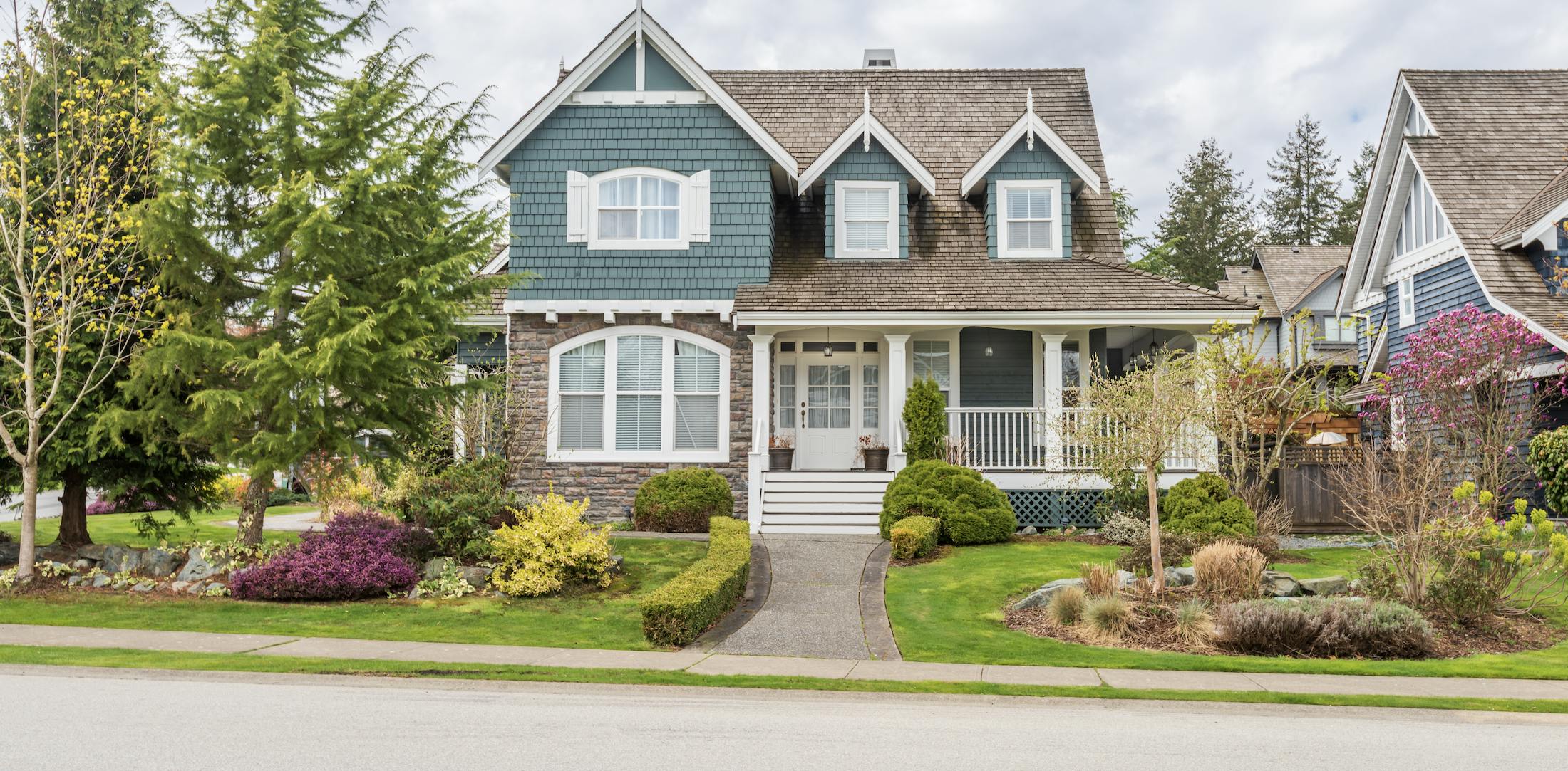 Teal and stone house with green grass, trees, and pink flowers