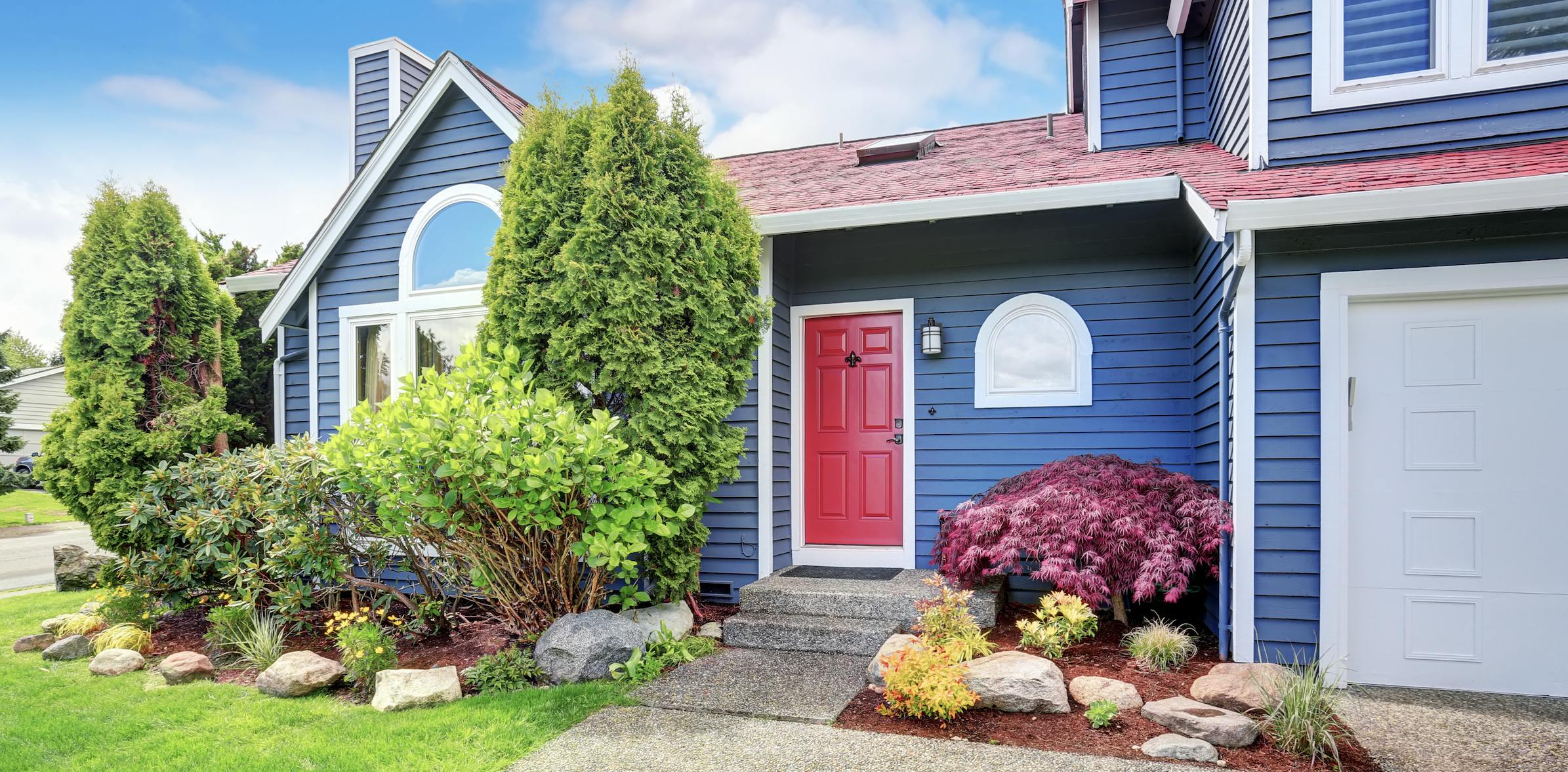 Blue house with red front door and green shrubbery