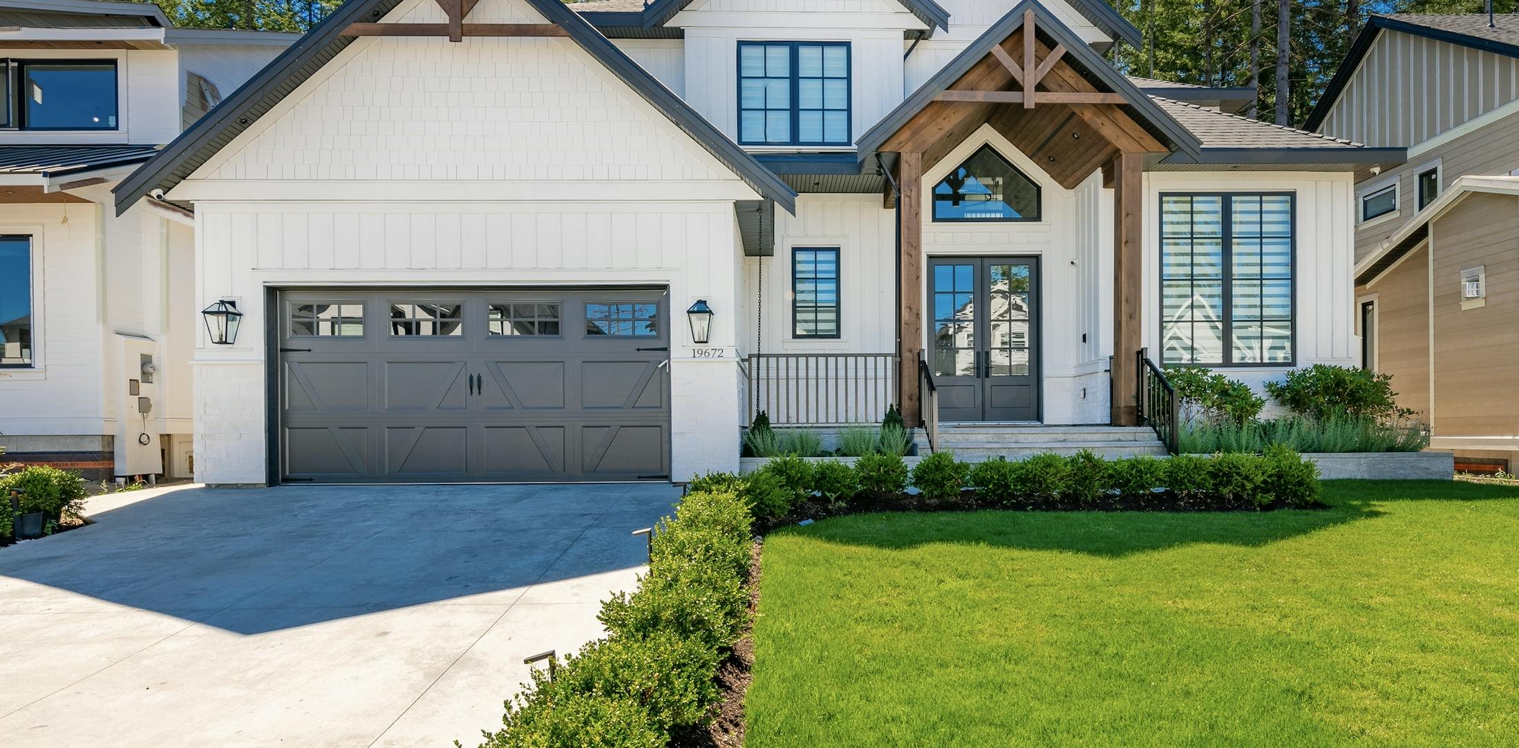 White house with black doors, wood trim, and green grass