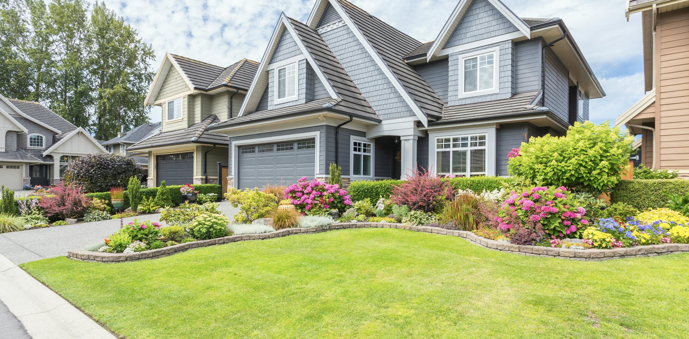 Gray house with green grass and flowers on a cloudy day