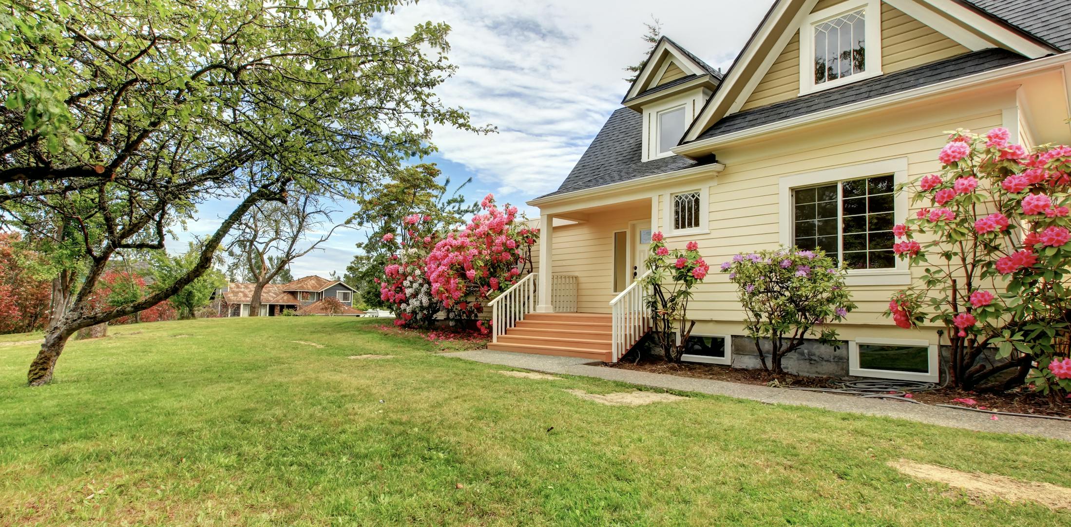 Yellow house with green grass and pink flowers