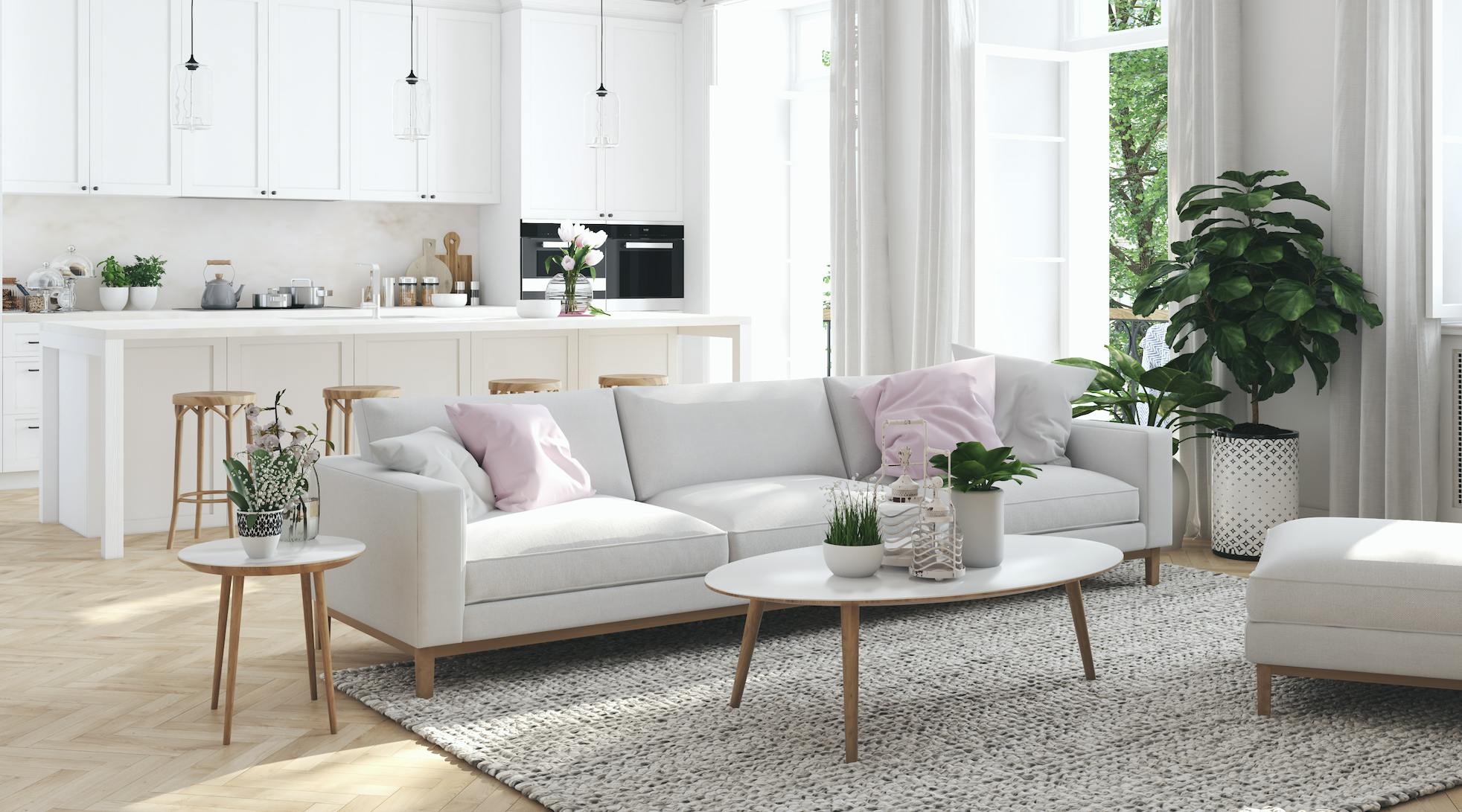 White kitchen in the background and living room in the foreground with beige sofa, pink accent pillows, and green plants dotted throughout.