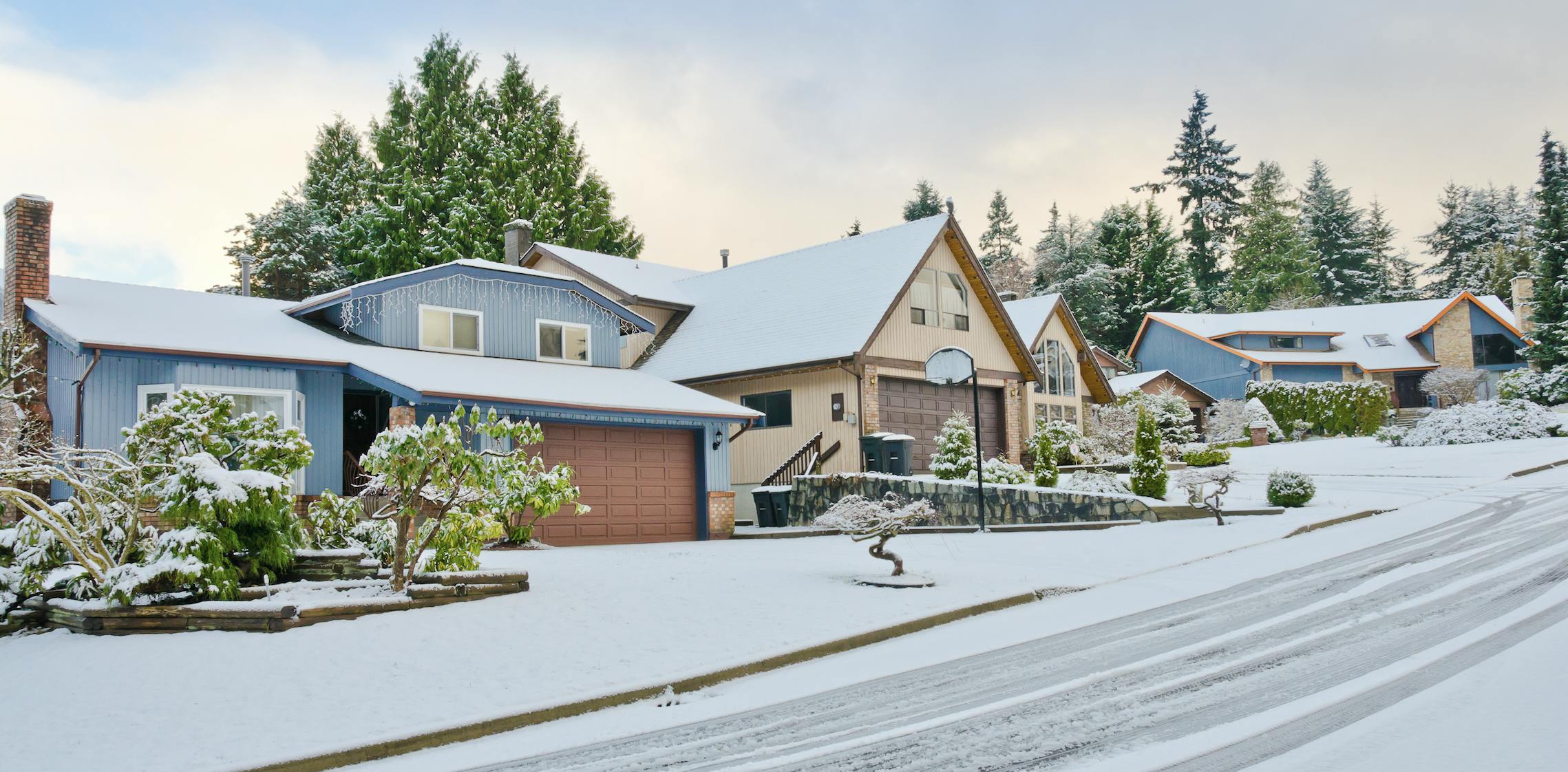 A blue and tan houses side by side on a snowy street