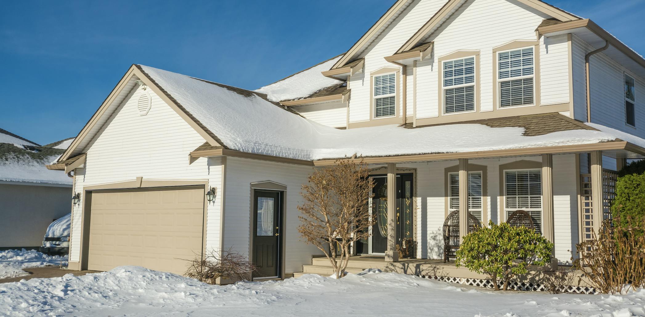 White house with beige trim, blue skies, and snow in the yard