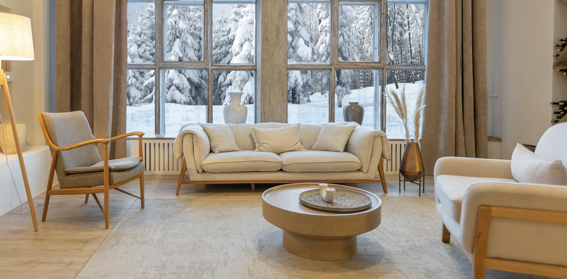 Home interior with neutral color furniture, a coffee table, lamp, and snow outside