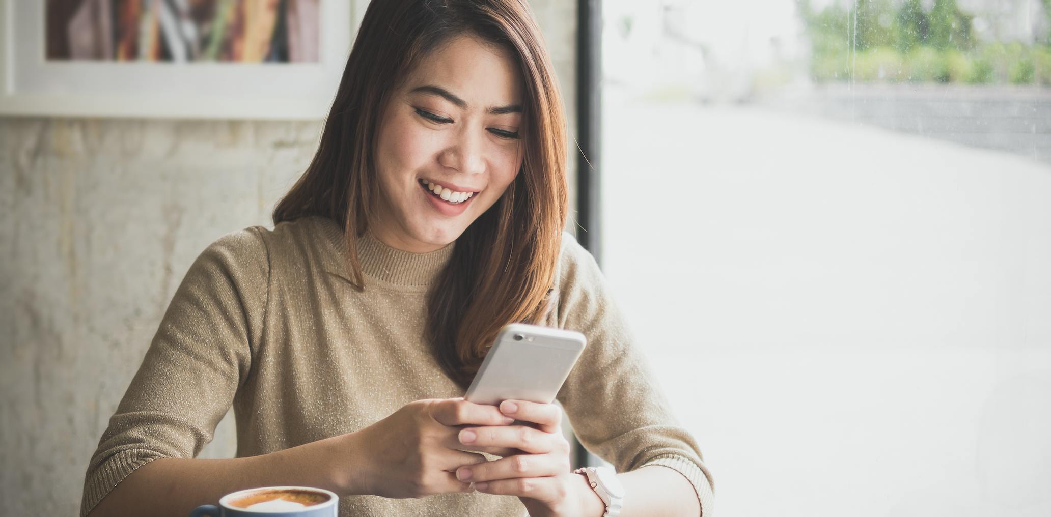Woman using smart phone in a cafe with a coffee mug.