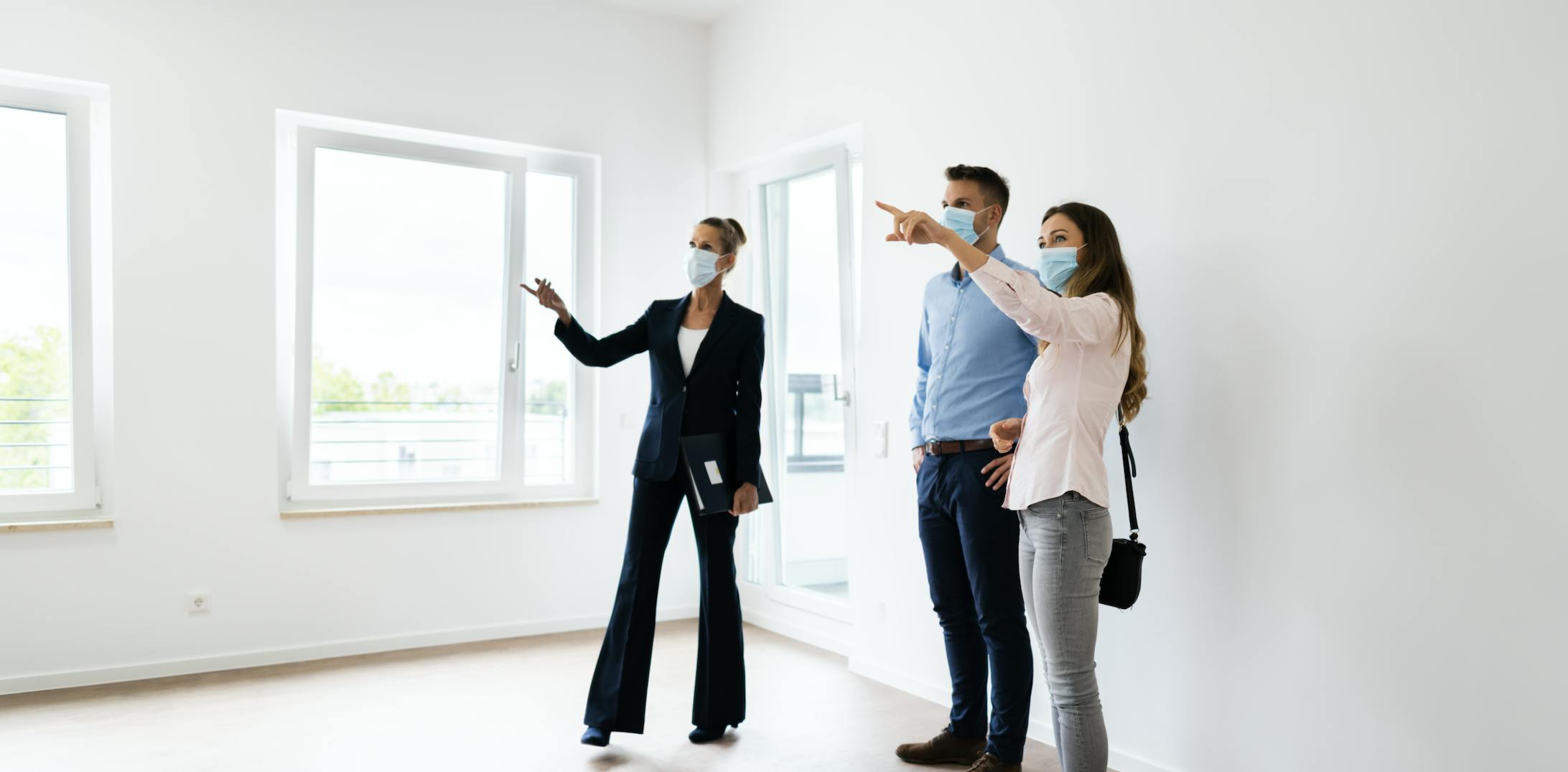 Two people are touring a house with a real estate agent. All three of them are wearing face masks.