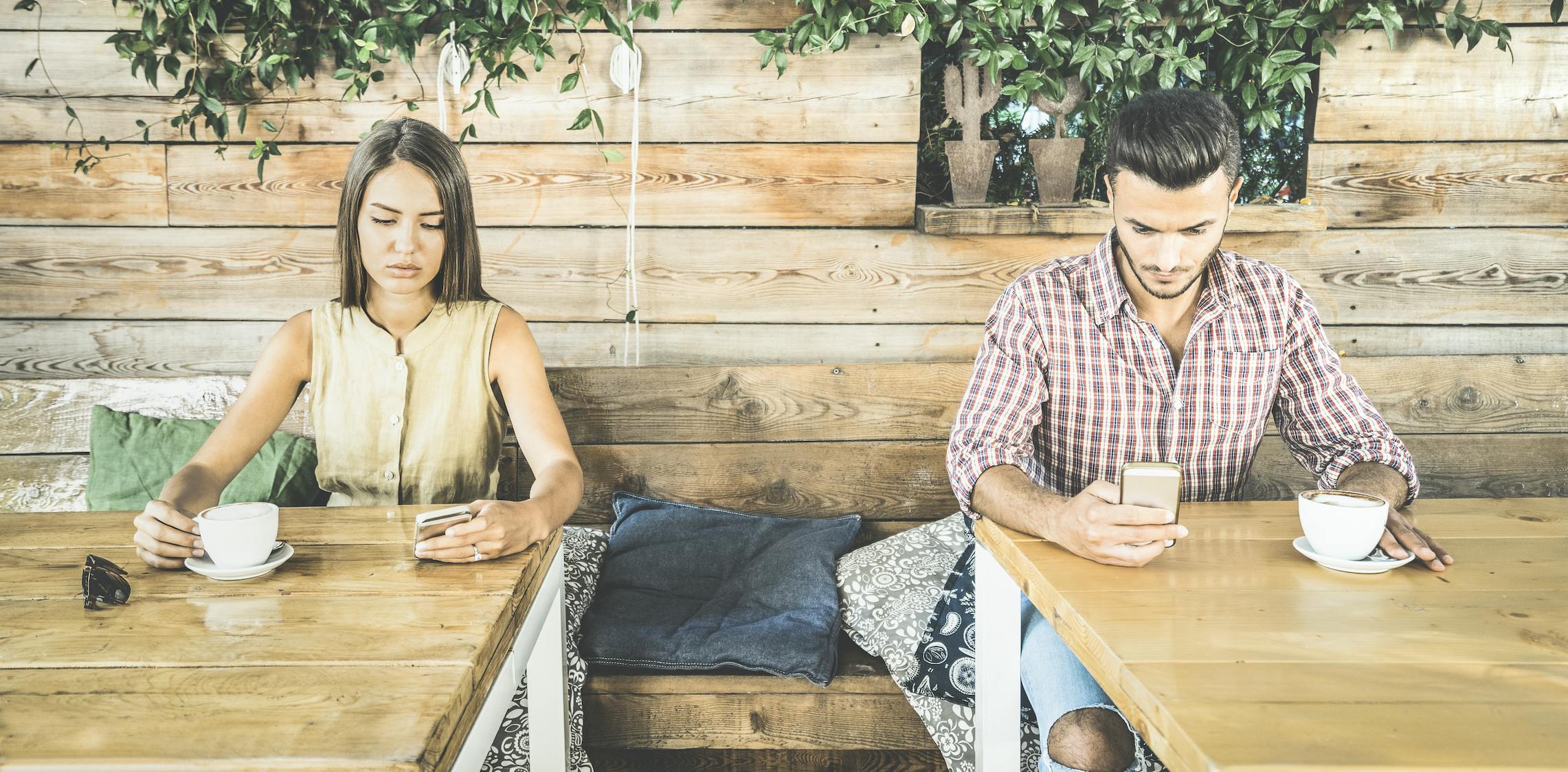 Two people sitting at separate tables on their smart phones.