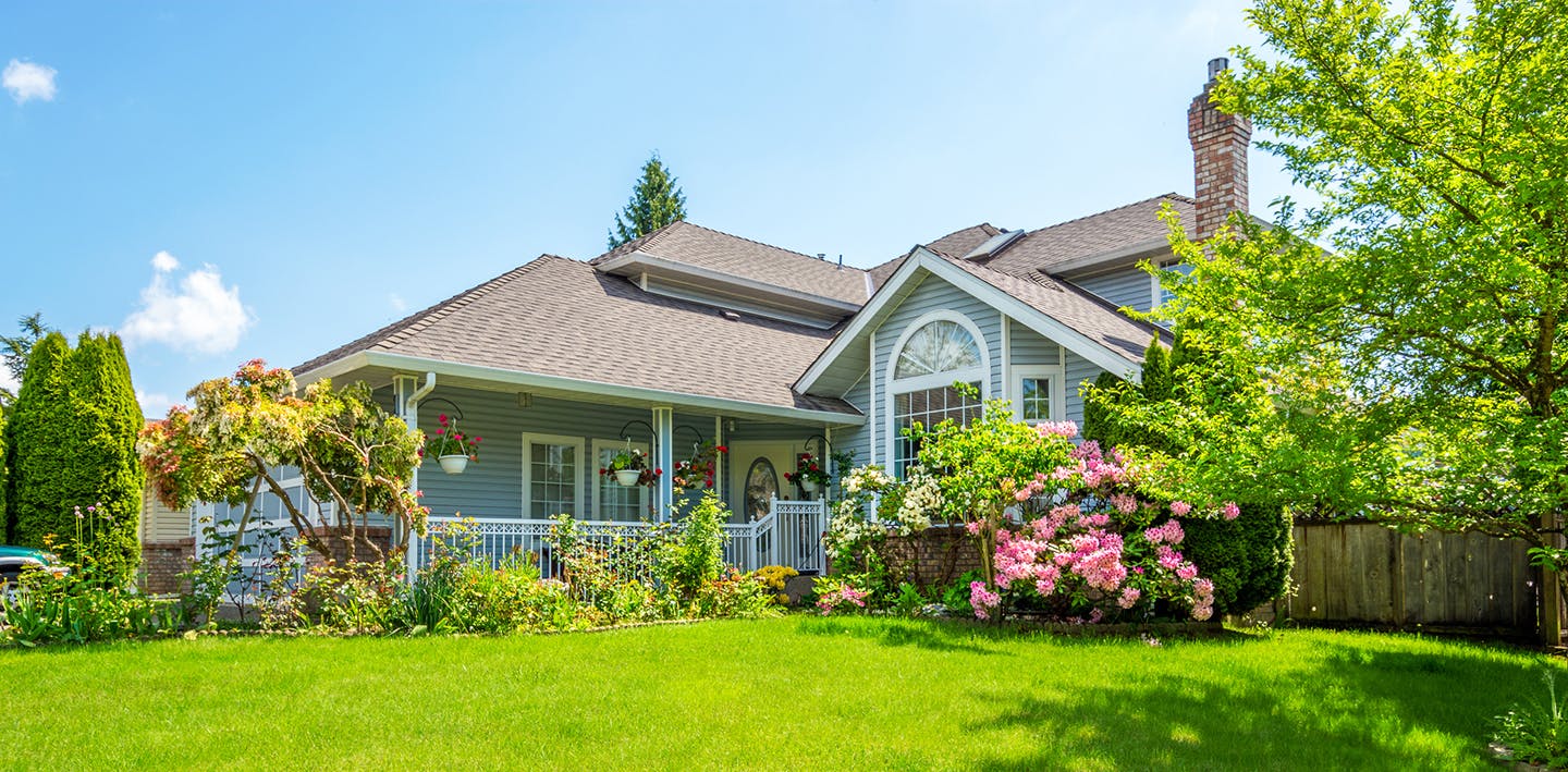 A blue house with green grass and plenty of flowers.